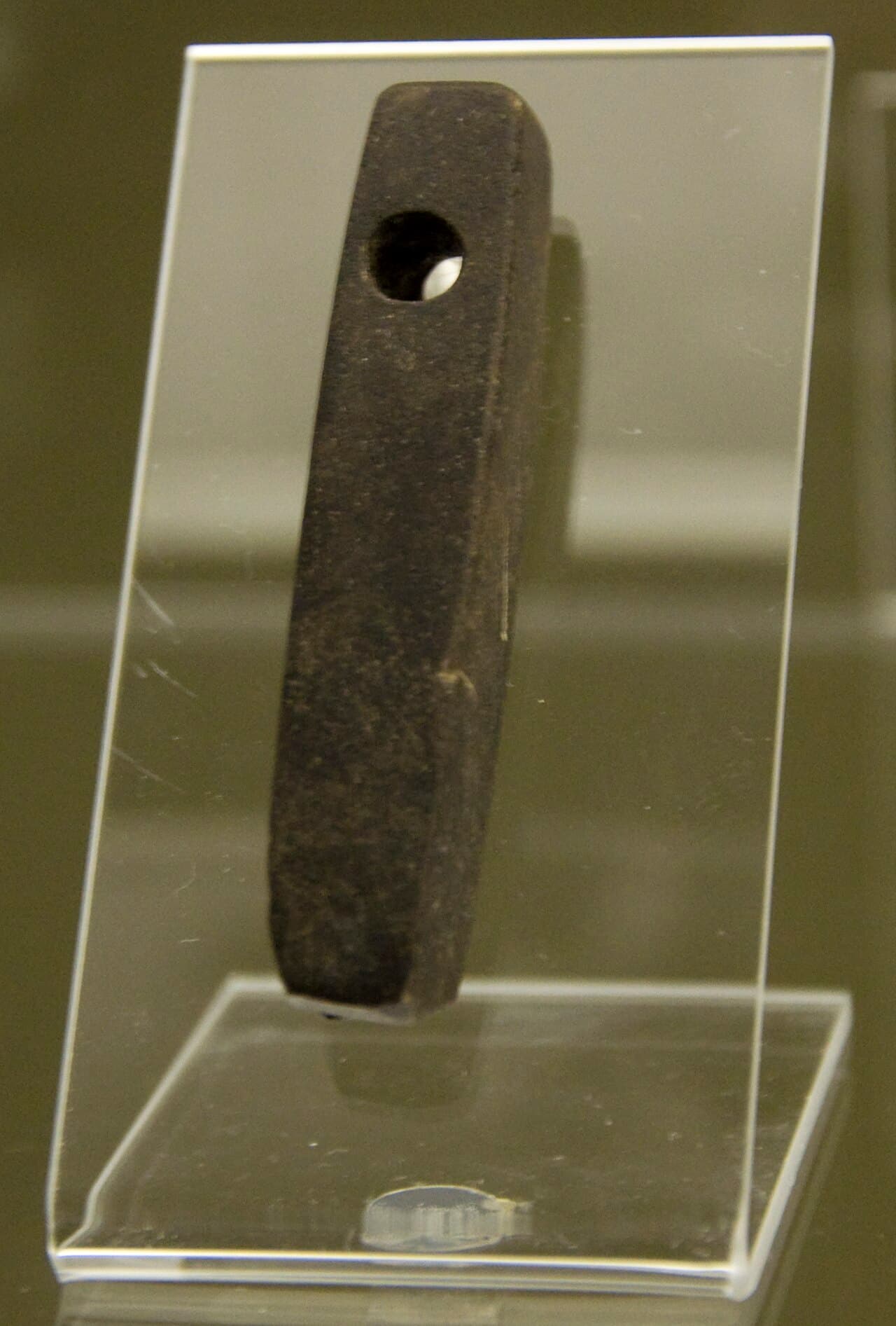 A narrow dark stone bar with a hole near one end, standing in a clear acrylic display holder.